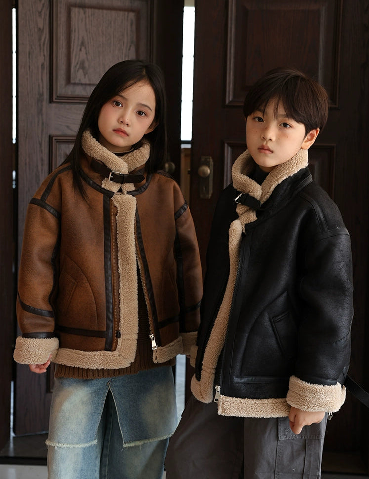 Two children wearing shearling jackets standing in front of a wooden door.