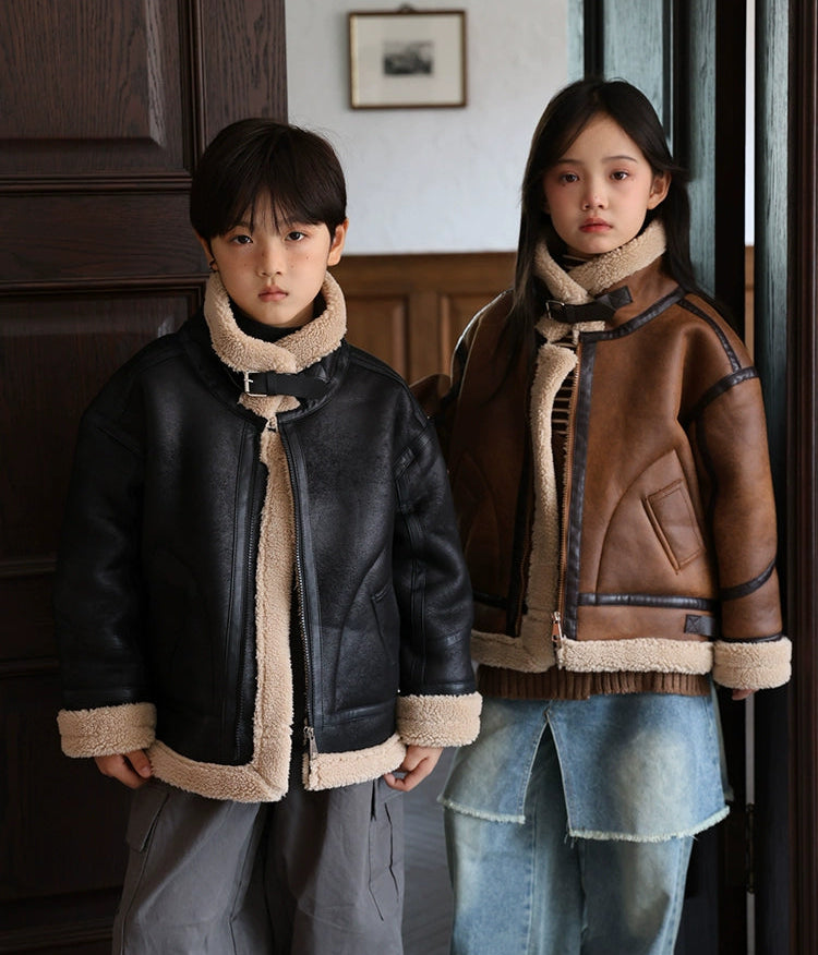 Two children wearing leather jackets with fur trim indoors.