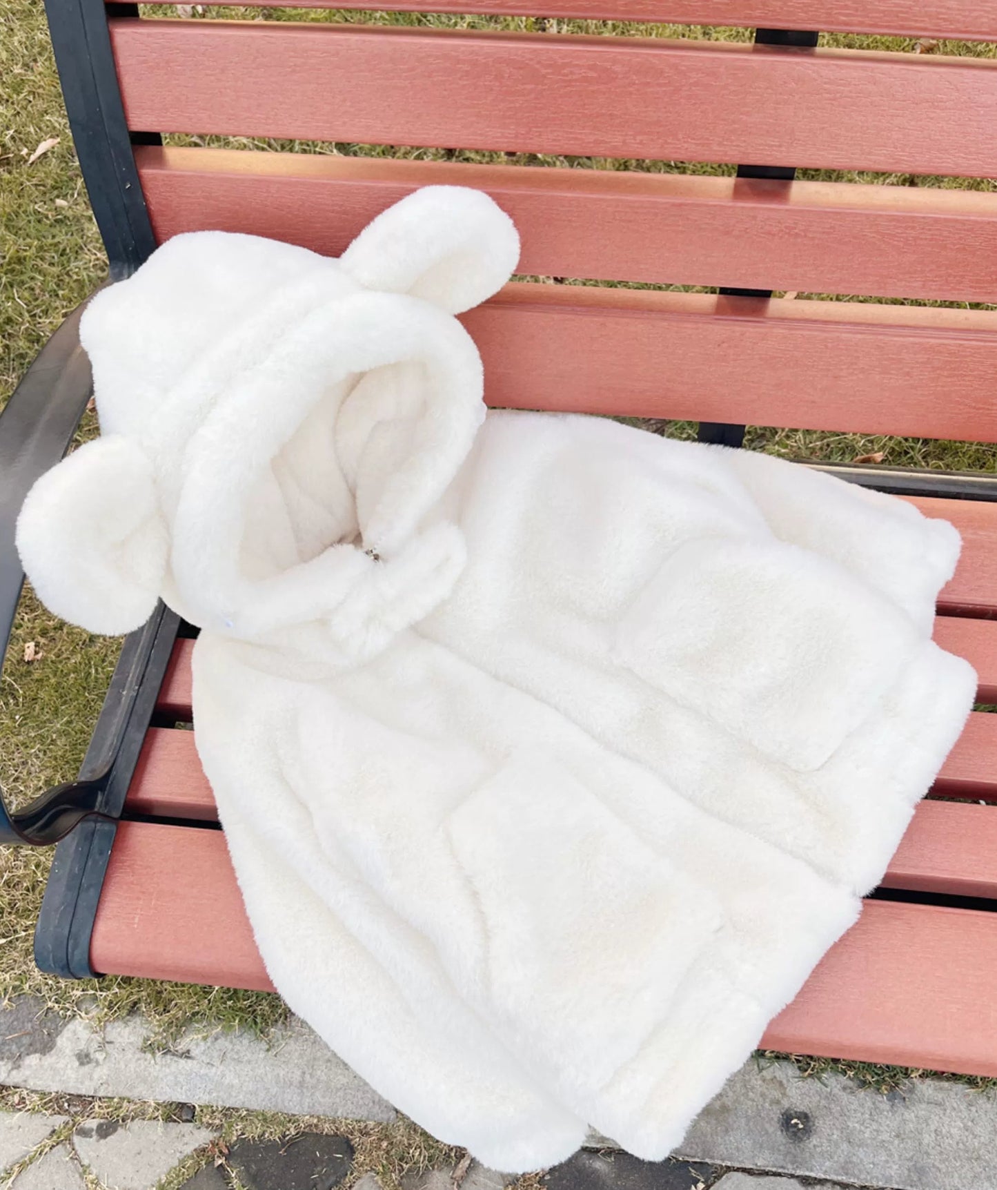 White fluffy blanket with bunny ears draped over a pink bench outdoors.