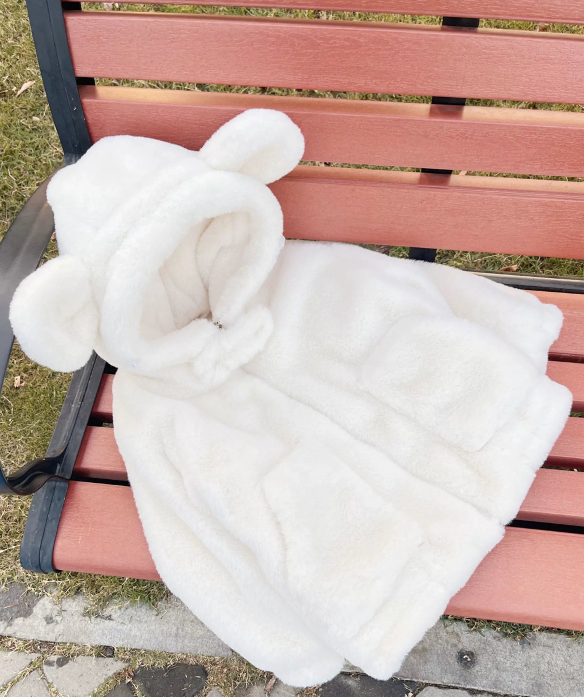 White fluffy blanket with bunny ears draped over a pink bench outdoors.