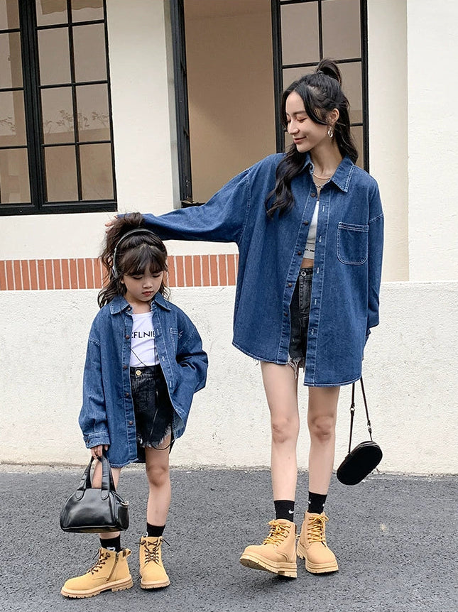 Two people, an adult and a child, wearing matching denim outfits with yellow boots in front of a building.