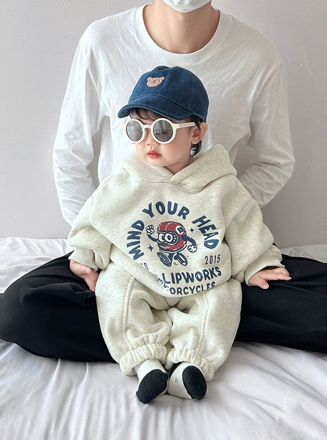 Child wearing a white hoodie with text and graphics, sitting on a bed.