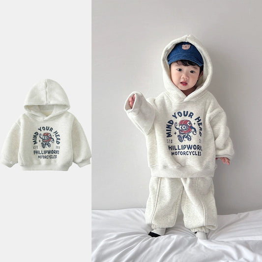 Child wearing a white hoodie with graphic design and text, standing on a bed.