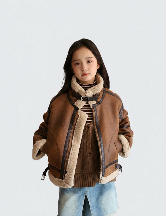 Person wearing a brown jacket with shearling collar and sleeves, standing against a light gray background.