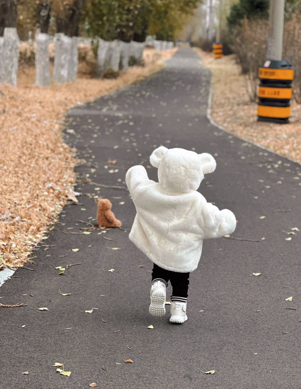 Child in a white bear costume running on a path with a teddy bear.