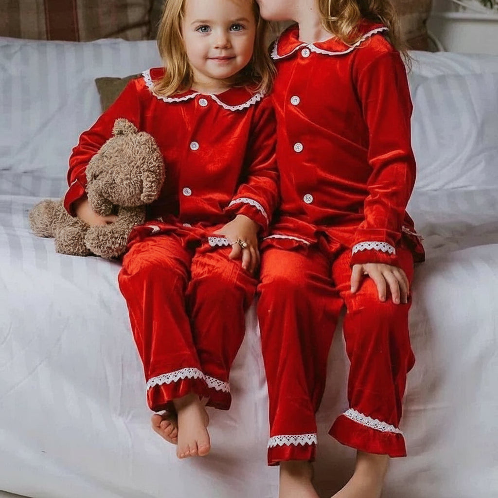 Two children in red pajamas sitting on a bed with one holding a teddy bear.