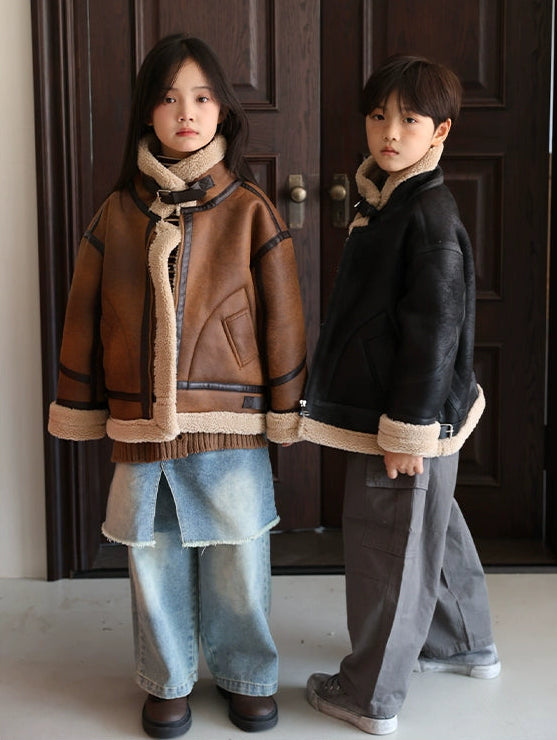 Two children wearing shearling jackets standing in front of a wooden door.