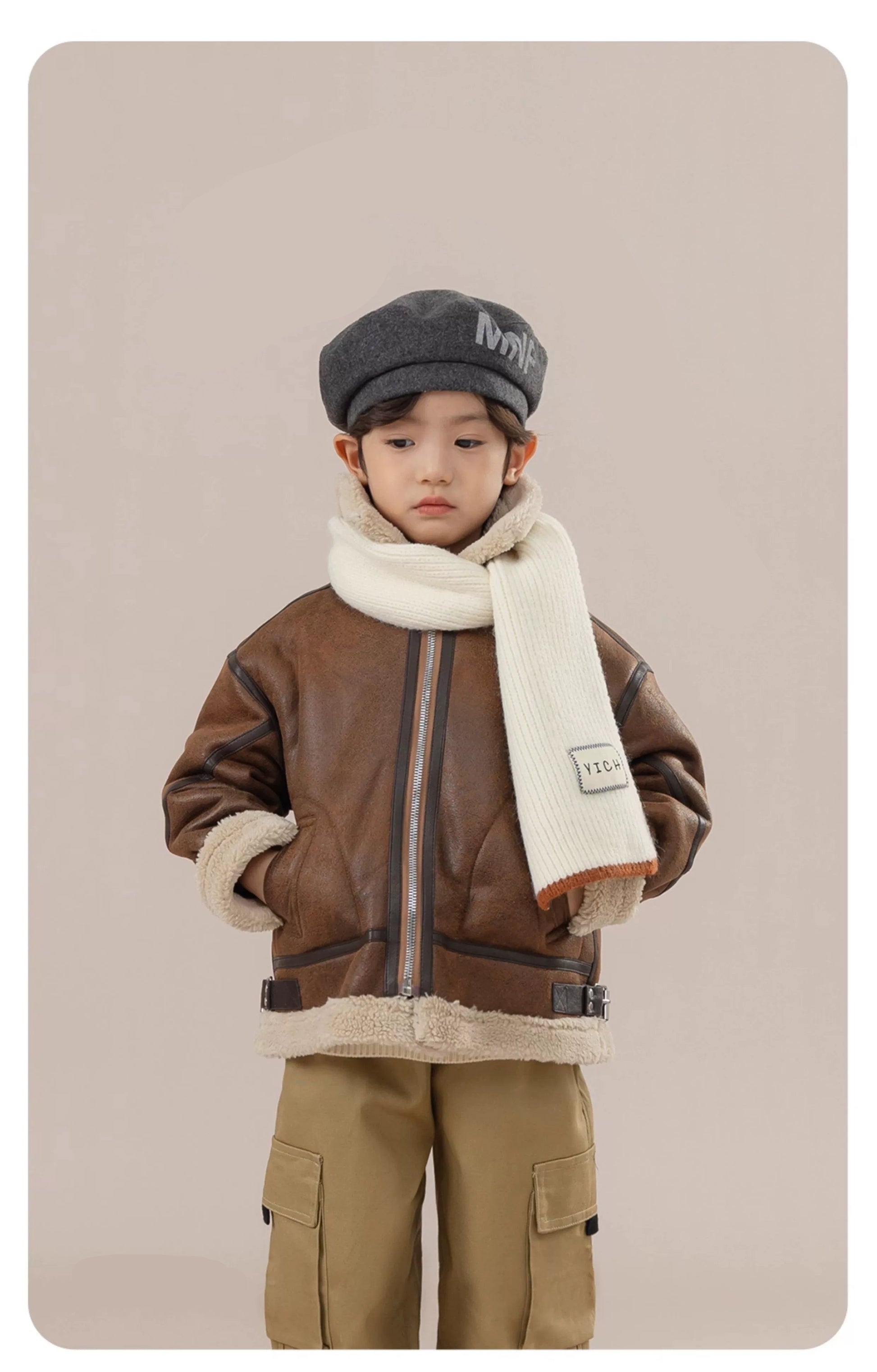 Child wearing a brown jacket, gray cap, and beige scarf on a beige background