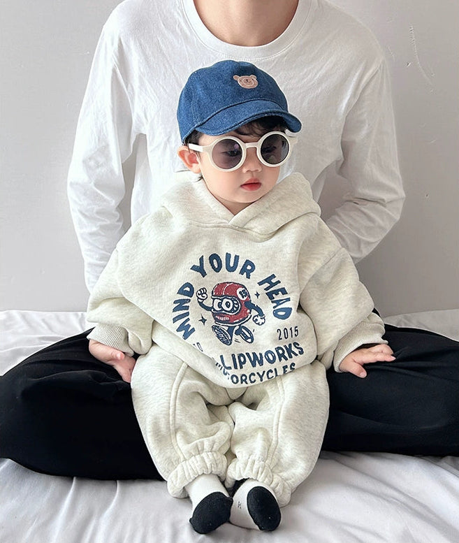 Child wearing a white hoodie with text and graphics, sitting on a bed with an adult.