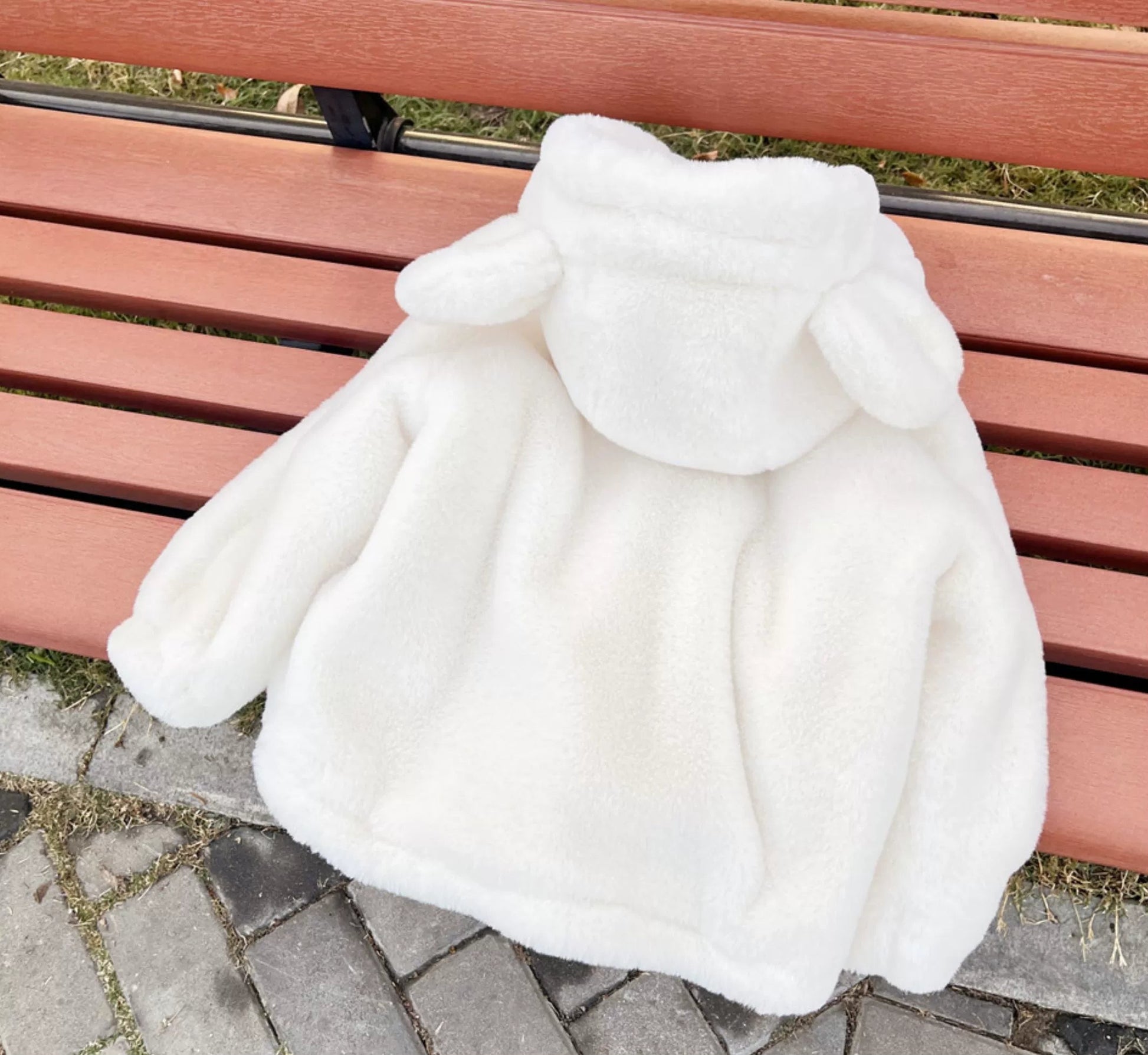 White baby coat on a pink bench outdoors.