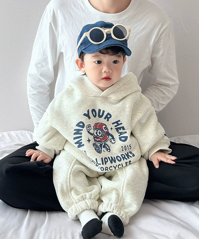 Child wearing a white hoodie with text and graphics, sitting on a bed.