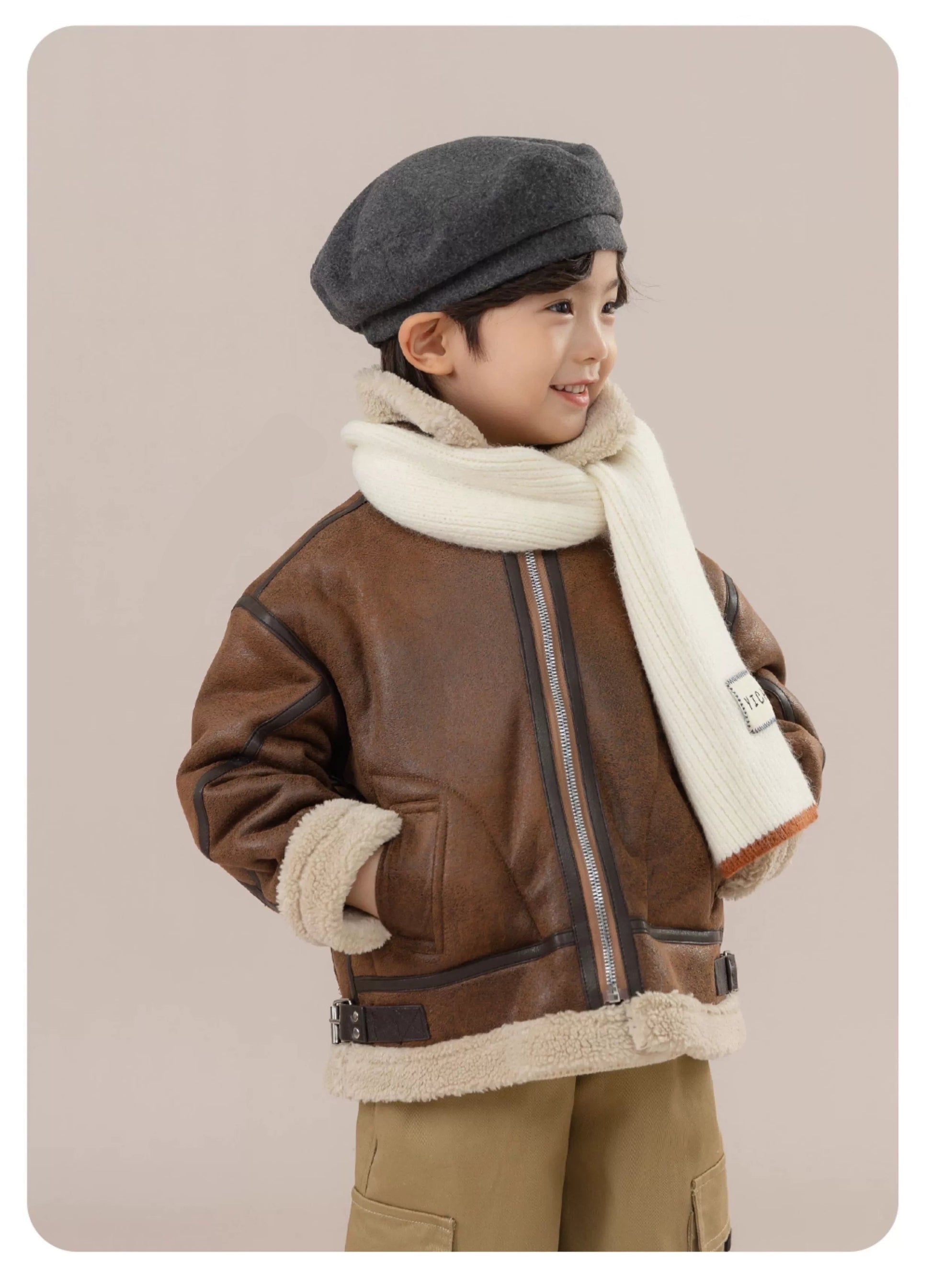 Child wearing a brown leather jacket with fur lining, gray cap, and white scarf on a beige background.