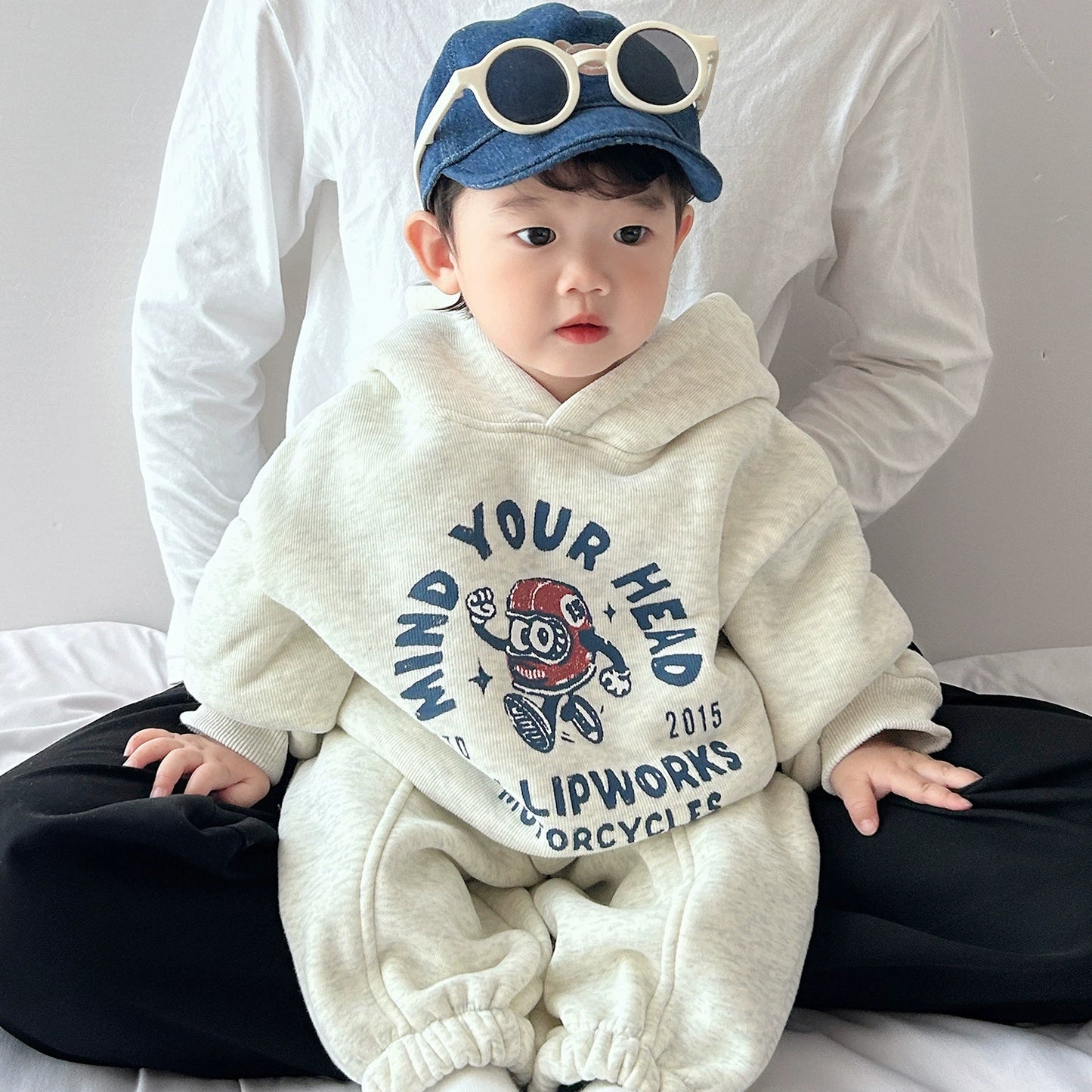Child wearing a white hoodie with text and graphics, sitting on a bed.
