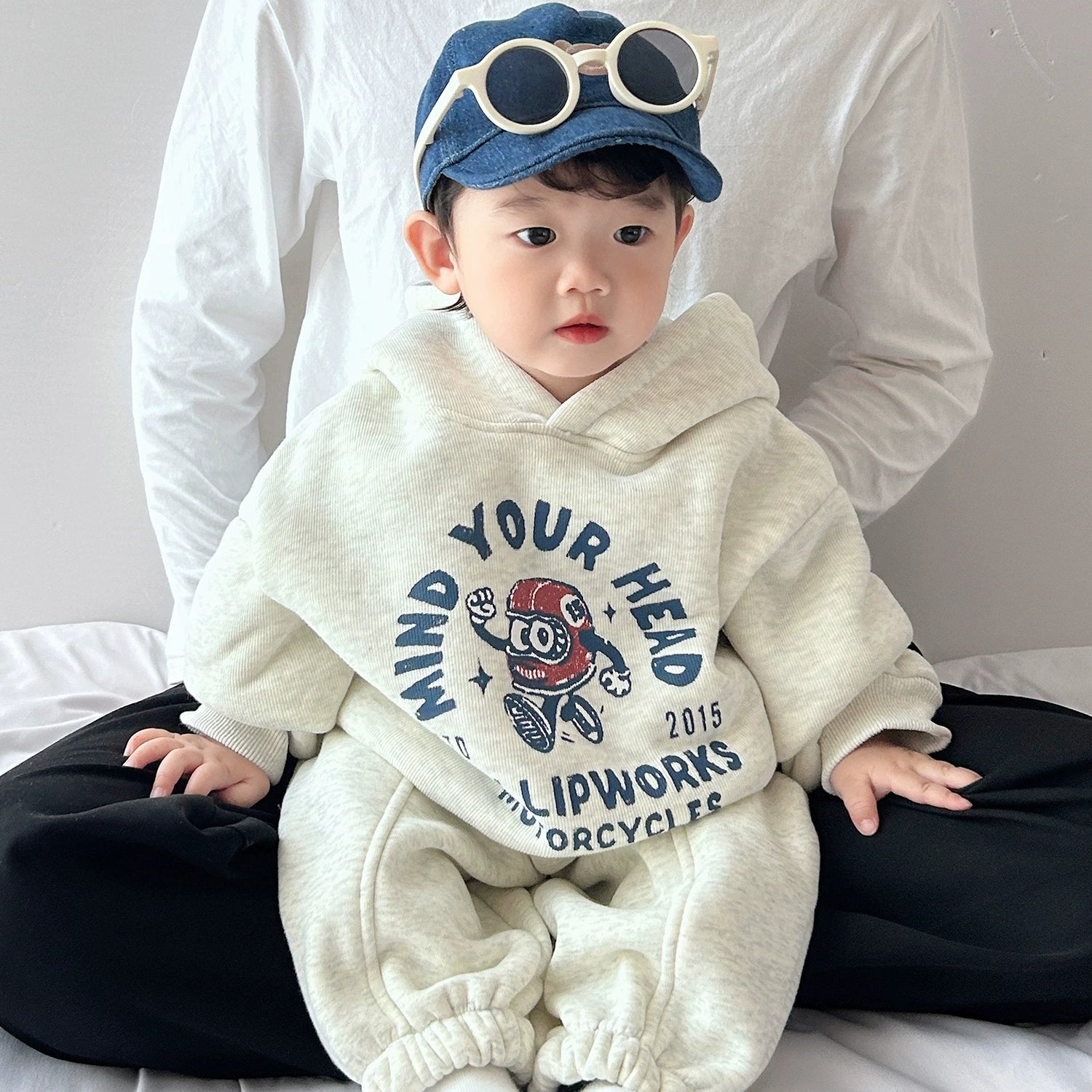 Child wearing a white hoodie with text and graphics, sitting on a bed.