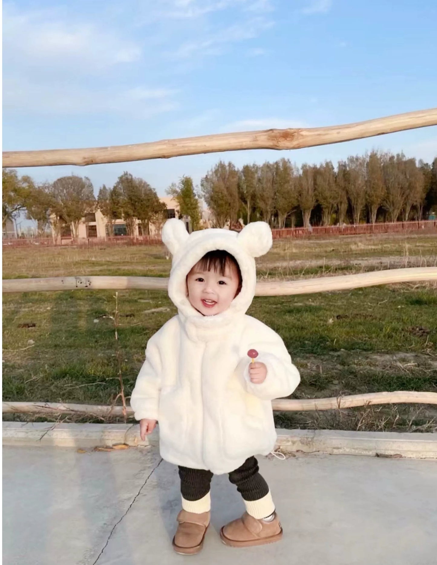 Child wearing a white bear-themed coat outdoors on a sunny day