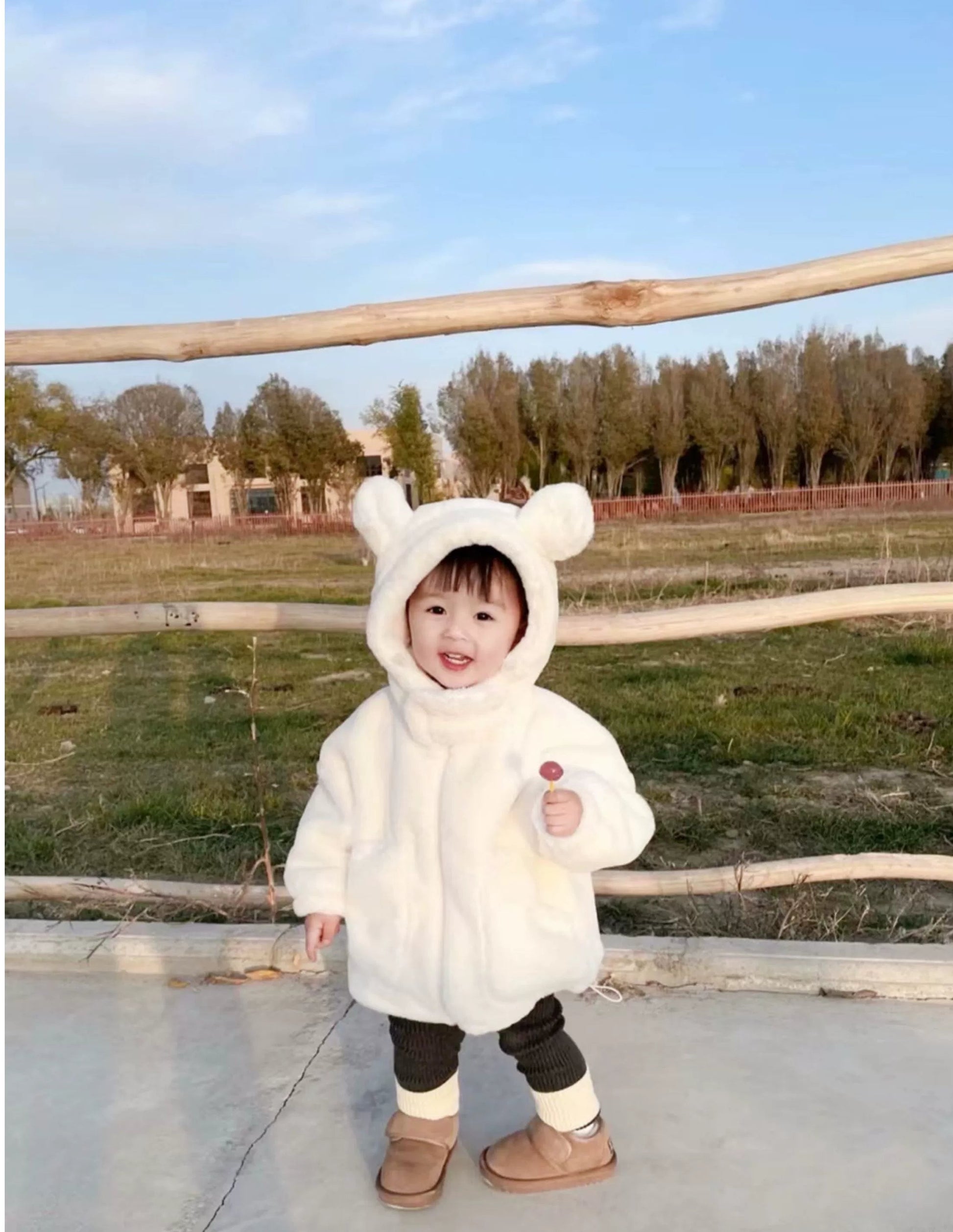 Child wearing a white bear-themed coat outdoors on a sunny day