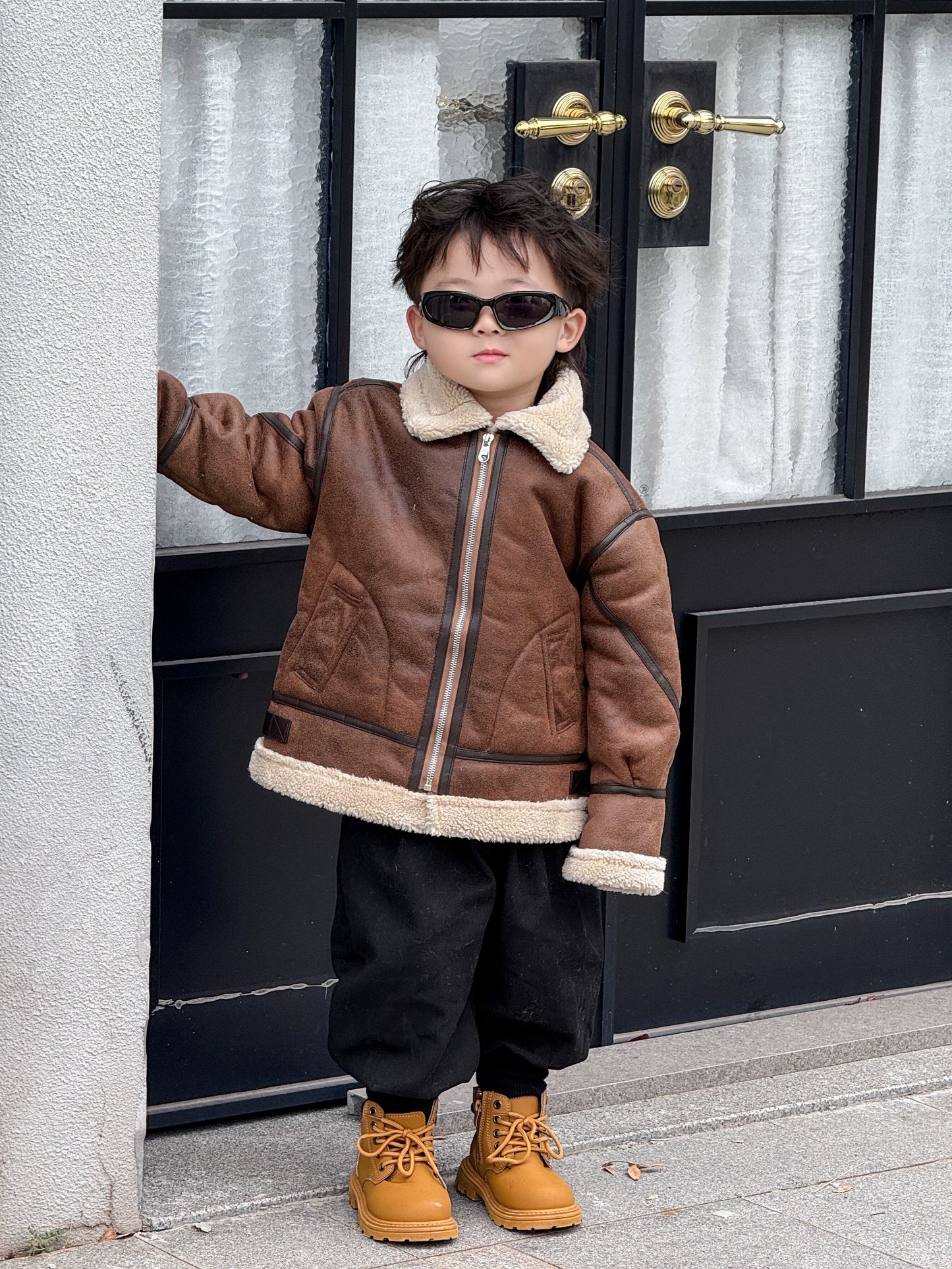 Child wearing a brown jacket with white fur trim, black pants, and tan boots standing in front of a door.