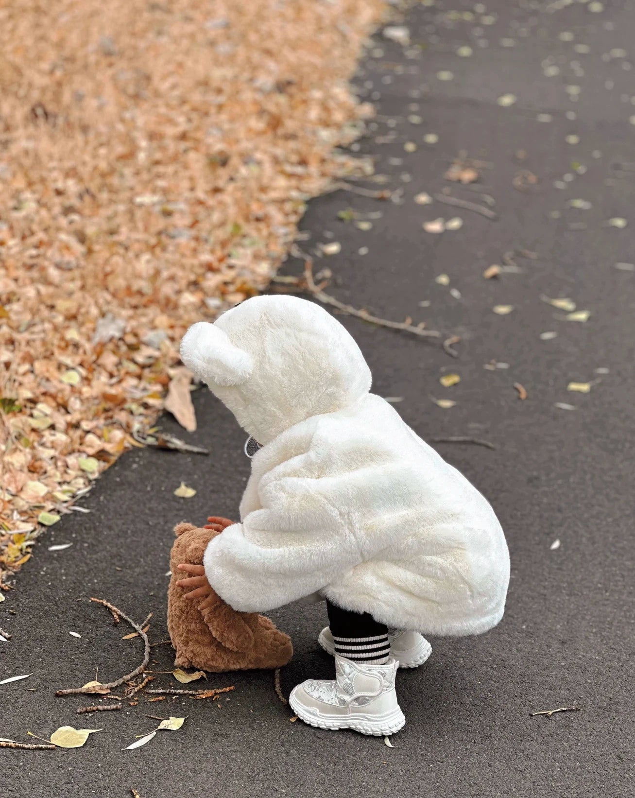 Person in a white bear costume crouching on a path with leaves and water.