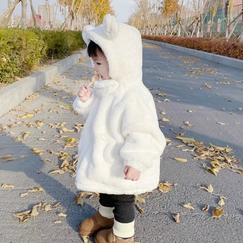 Child wearing a white fluffy coat with bear ears on a sidewalk with fallen leaves.