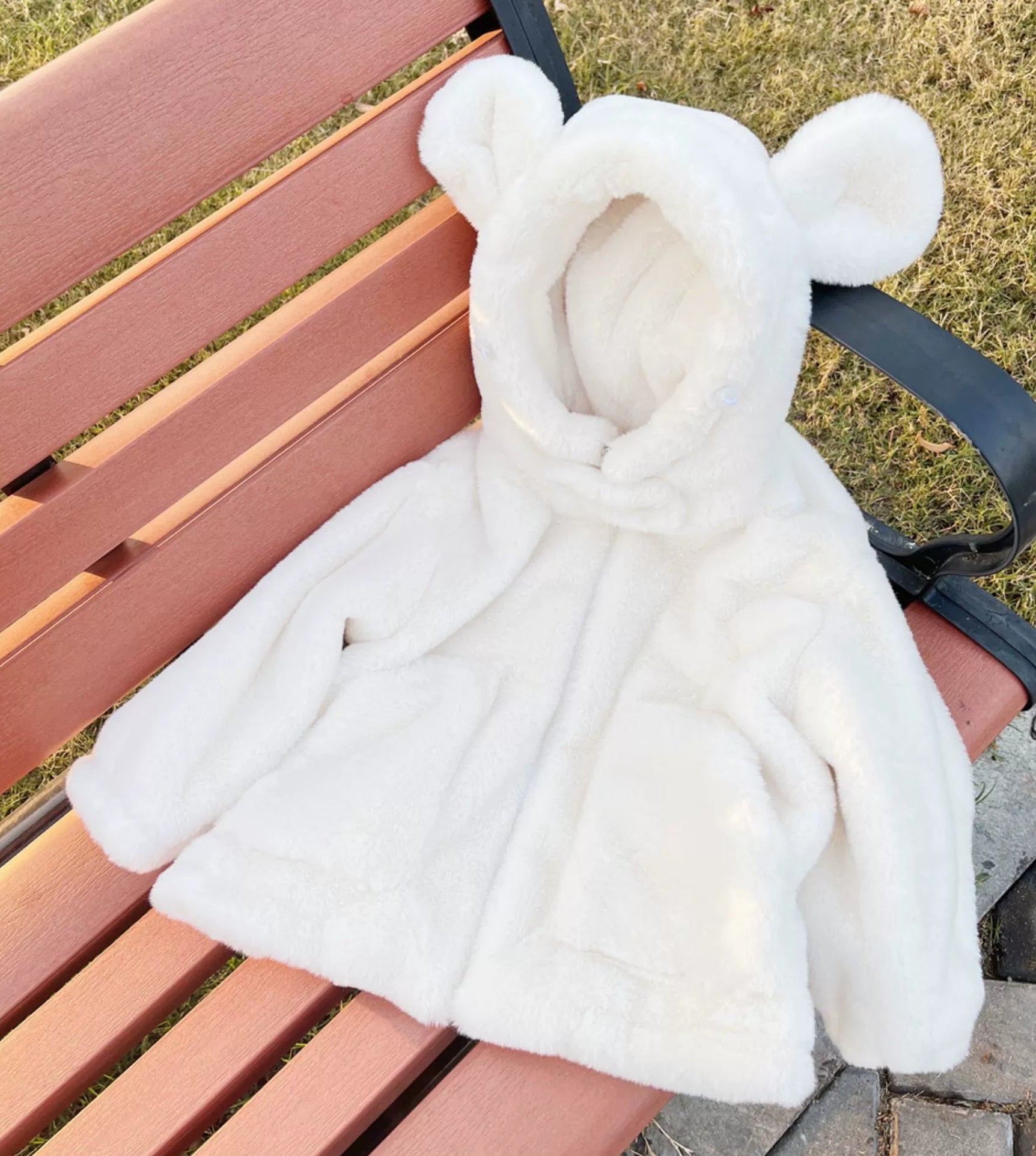 White fur coat with bear ears on a pink bench outdoors