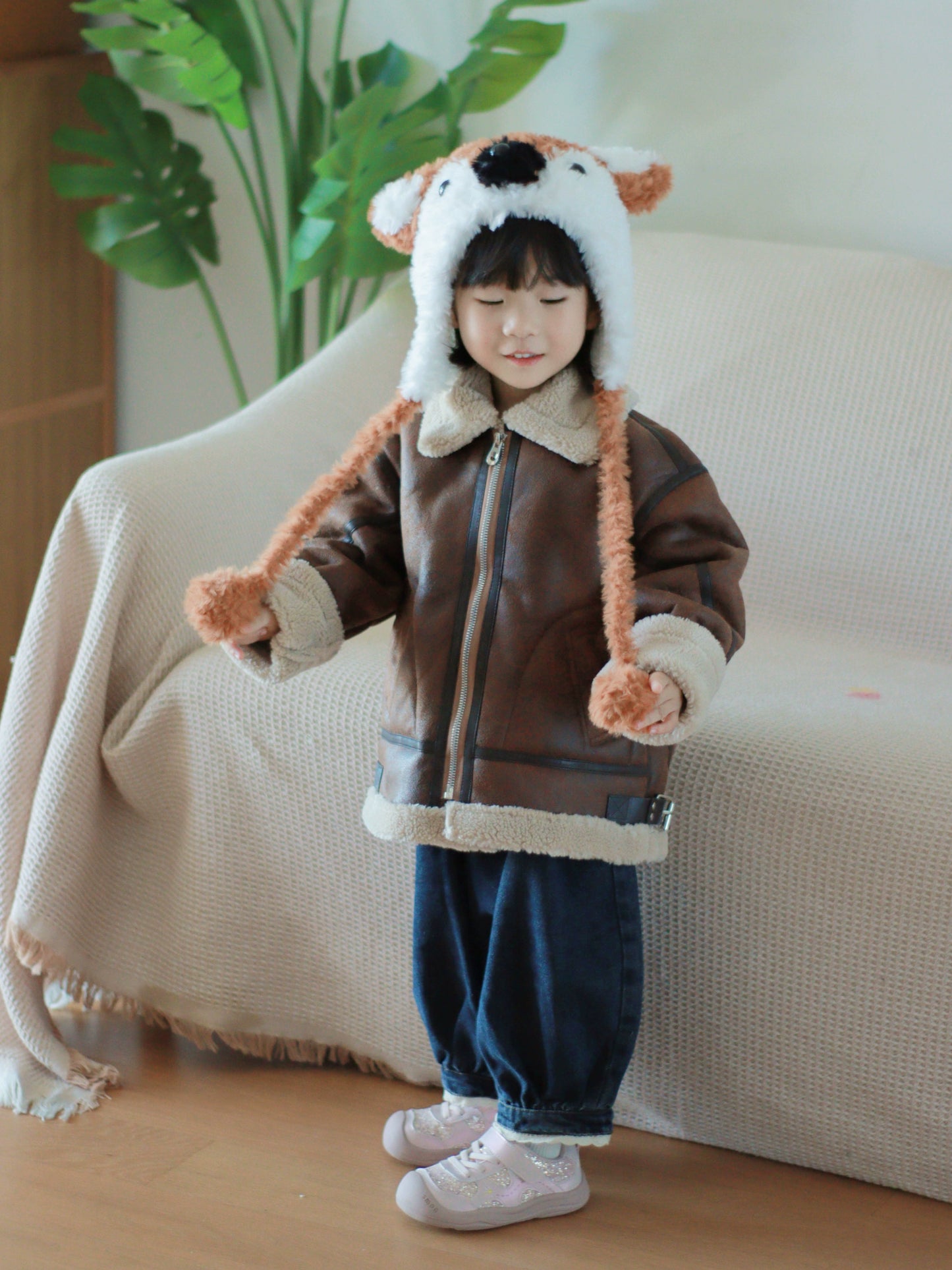 Child wearing a brown jacket with a fox hat in a cozy indoor setting