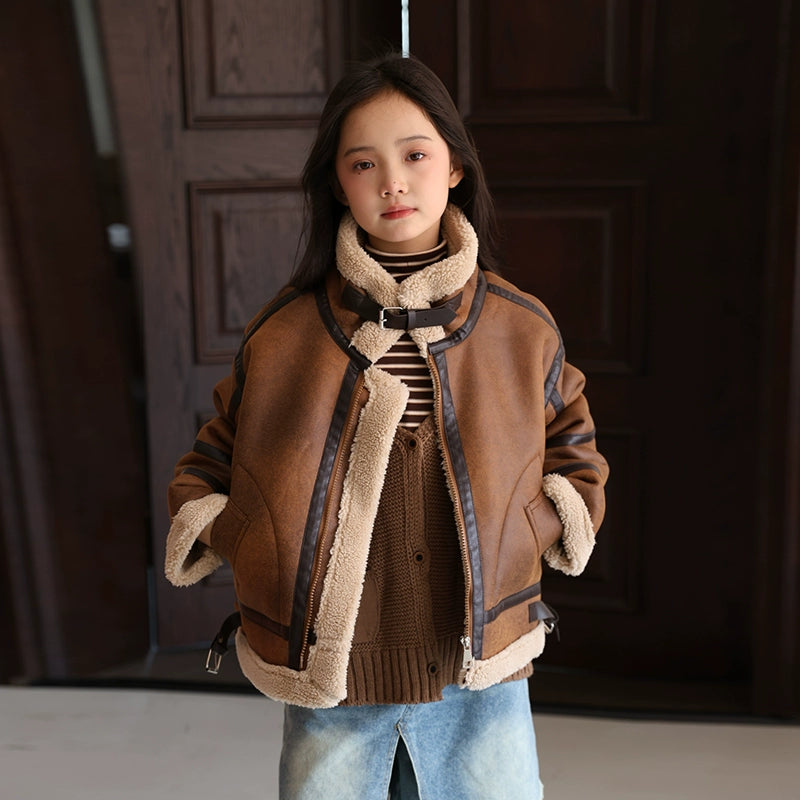 Person wearing a brown jacket with shearling trim in front of a dark door.