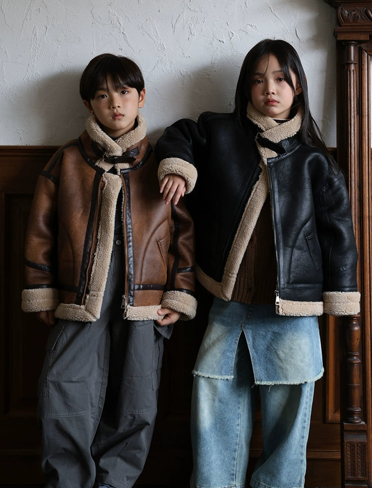 Two individuals wearing shearling jackets in a room with wooden furniture.