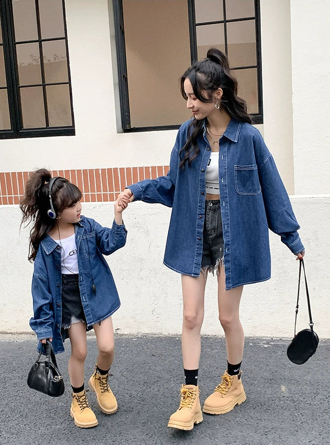 Two people, likely a mother and daughter, wearing matching denim jackets and holding hands outdoors.