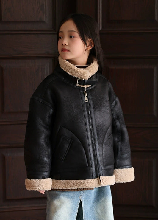 Person wearing a black leather jacket with beige trim against a dark wooden panel background