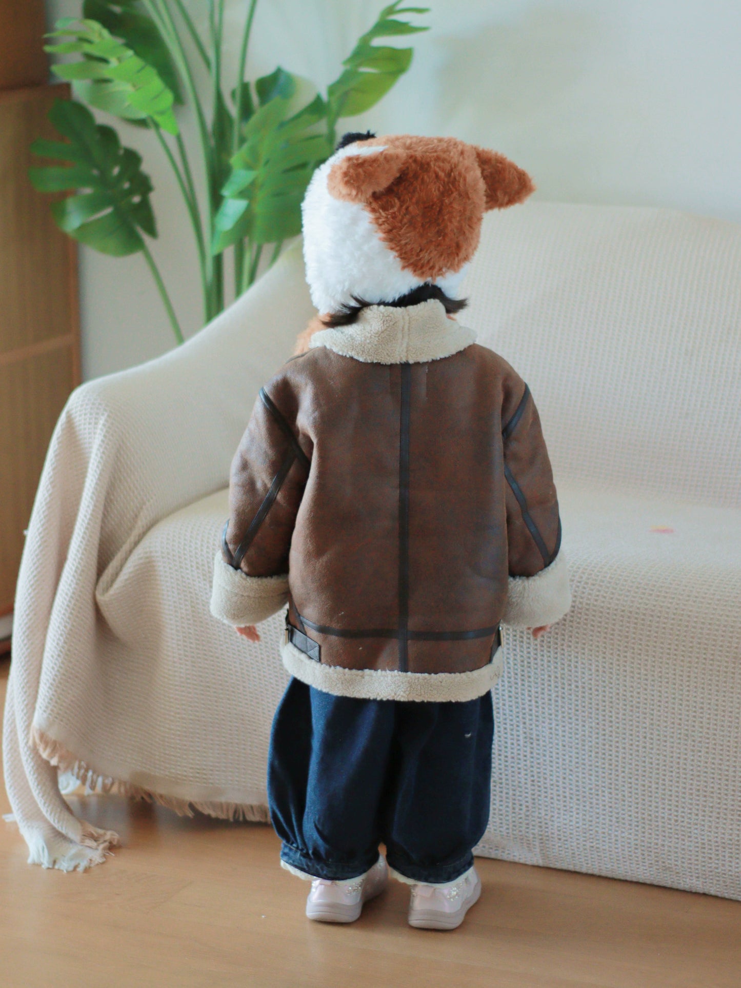 Child wearing a brown jacket and fox hat standing in front of a white couch.