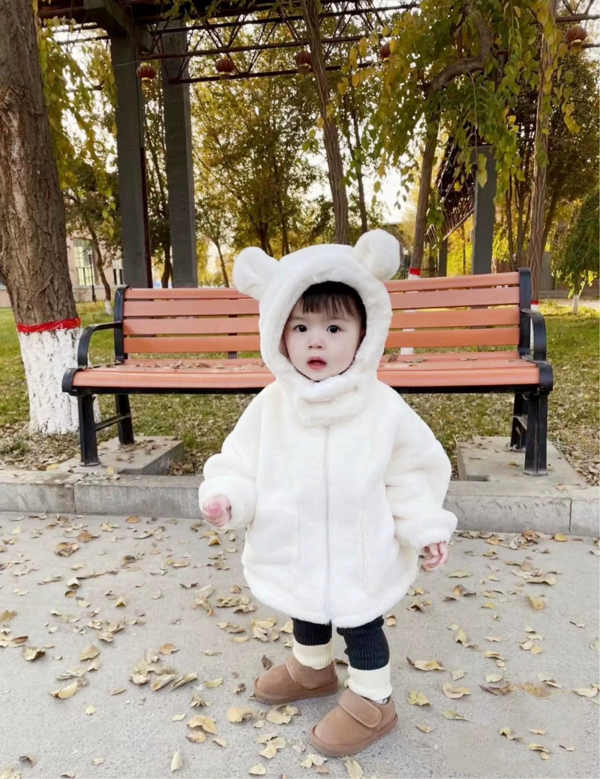 Child wearing a white bear-themed coat in a park setting